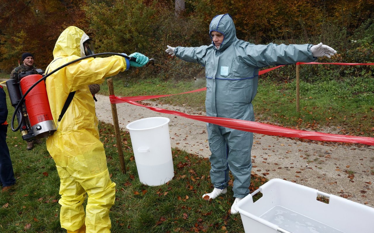 Die Personen in der roten Zone werden von anderen Menschen in gelber Schutzbekleidung von Kopf bis Fuss desinfiziert.