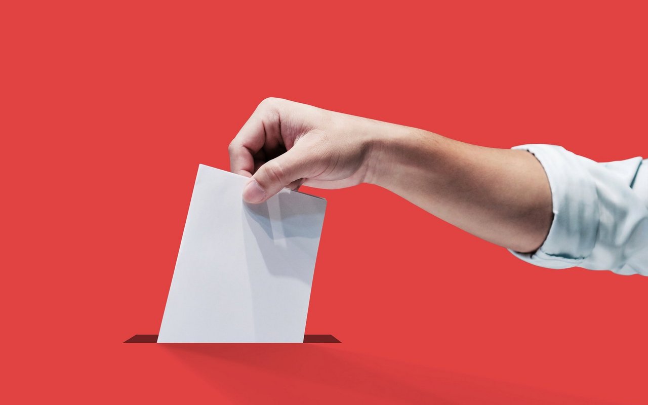 Symbolbild einer Hand, welche einen Stimmzettel in die Urne wirft.