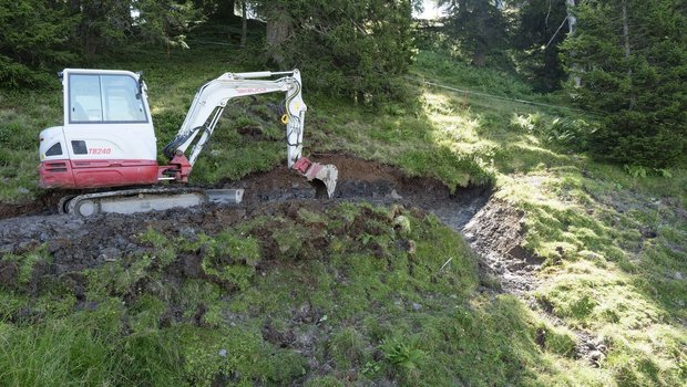 Wasserversorgung Alpwirtschaft Ein Bagger steht im Hang, daneben gluckert ein kleines Wasserrinnsal hinunter.