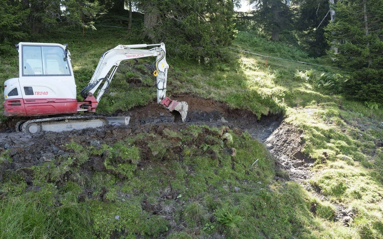 Ein Bagger steht im Hang, daneben gluckert ein kleines Wasserrinnsal hinunter.