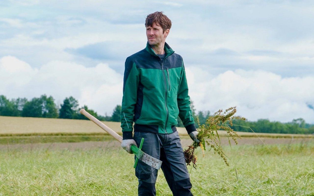 Kilian Baumann steht in Arbeitskleidung auf einem Feld.