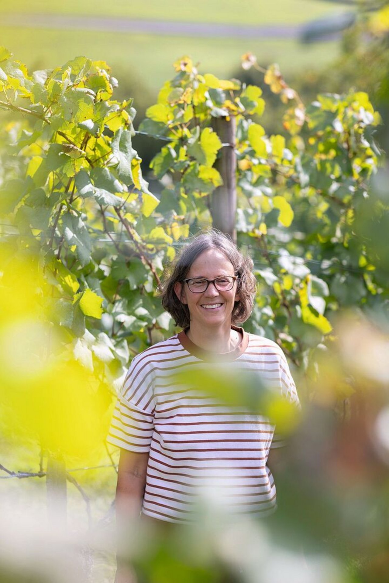 Barbara Thürig steht zwischen den Rebpflanzen und schaut in die Kamera.