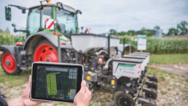 Swiss Future Farm Im Hintergrund ist eine Sämaschine zu sehen, im Vordergrund halten zwei Hände ein Tablet.