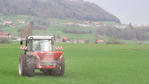 Mineraldünger Preise Ein Traktor fährt mit dem verteilenden Düngerstreuer über das Feld.
