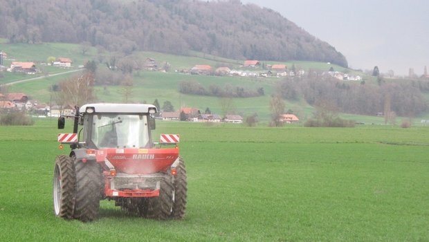 Ein Traktor fährt mit dem verteilenden Düngerstreuer über das Feld.