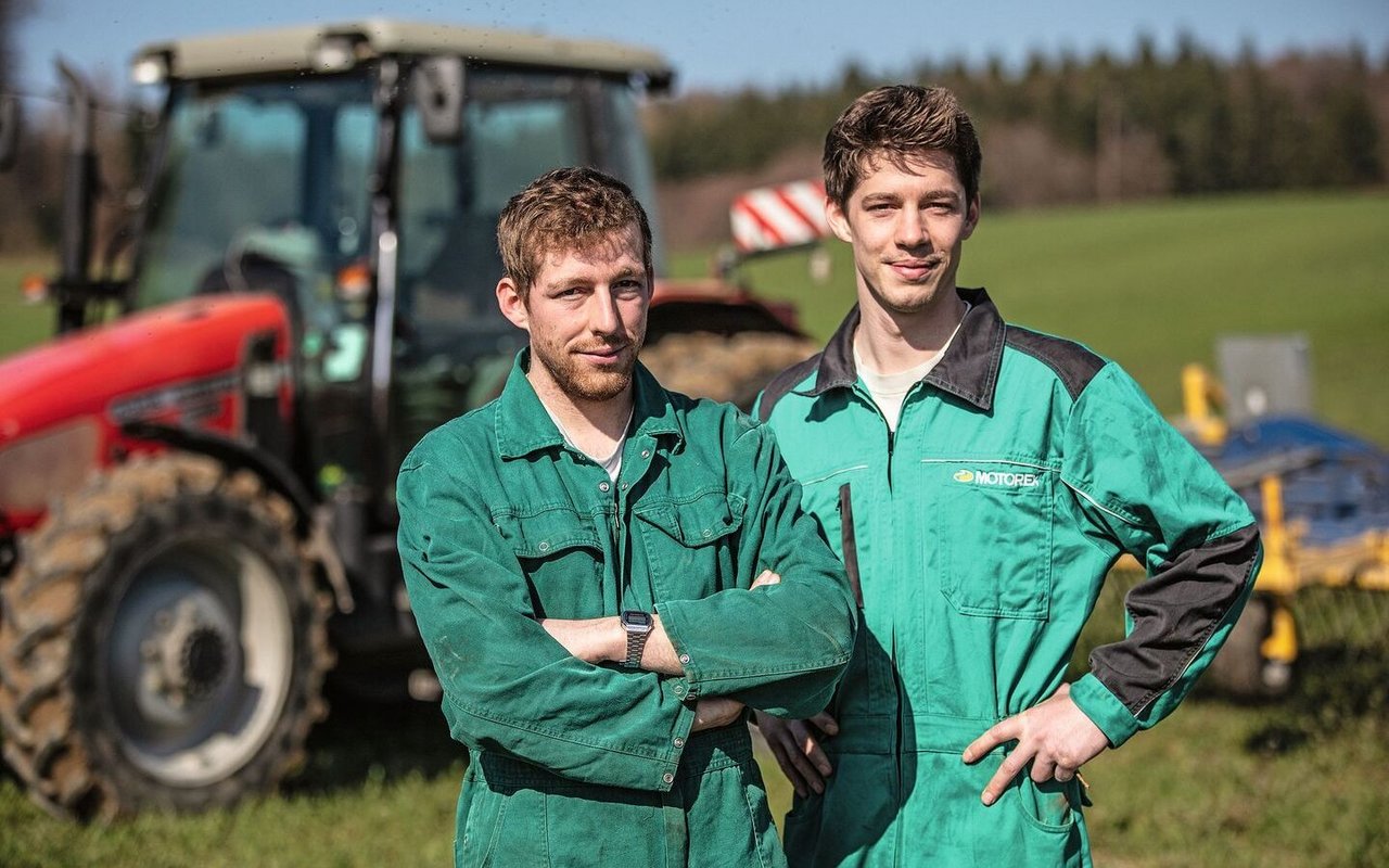 Die Brüder Ramseyer stehen im Overall vor dem Traktor auf dem Feld.