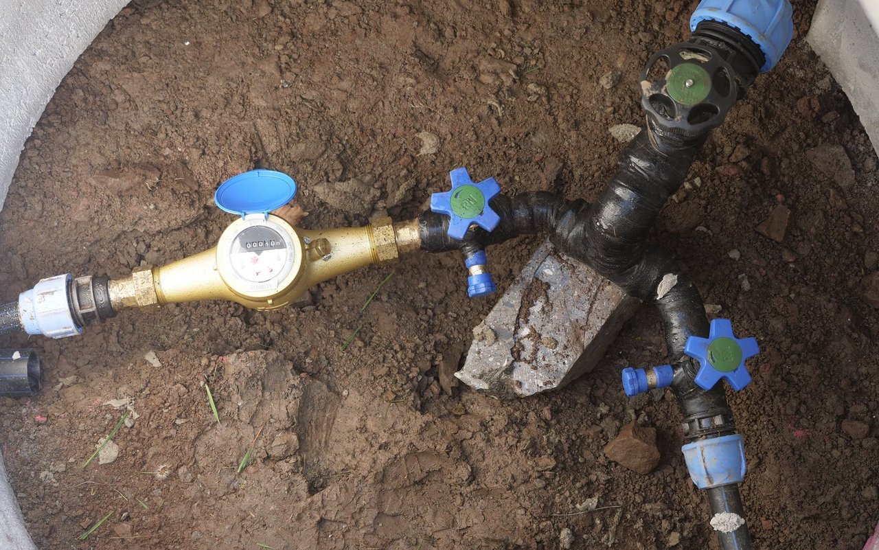 Blick von oben in einen Schacht: Von einer Leitung zweigen zwei ab, eine mit einer Wasseruhr versehen.