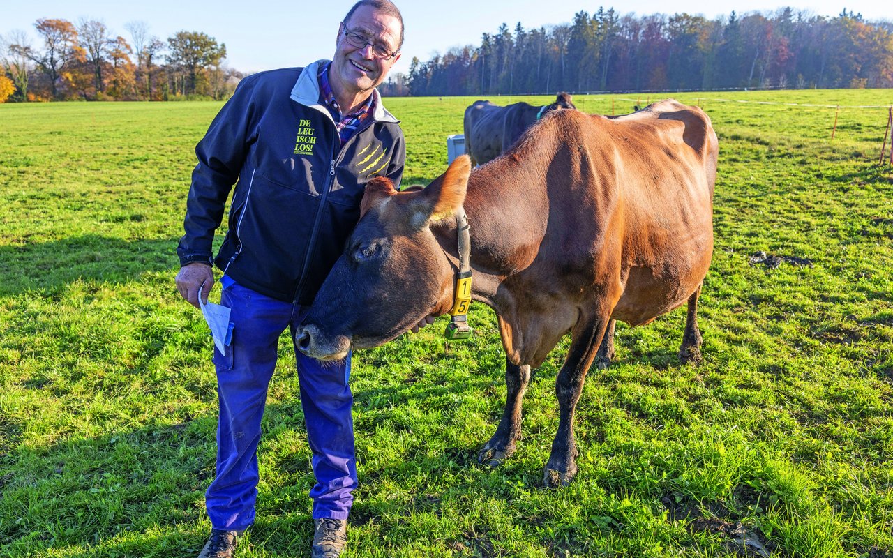 Ruedi Rutishauser steht auf der Weide und krault der Kuh den Hals.