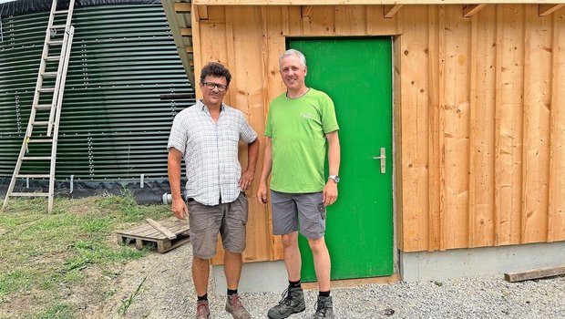 Rolf Mengelt und And Rolf Mengelt und Andreas Braun (v. l.) stehen vor dem Pumpenhäuschen. Hinter ihnen ist ihr grünes Wasserreservoir zu sehen, das von Grundwasser gespeist wird. Von dort wird das Wasser in ihre Felder geleitet.