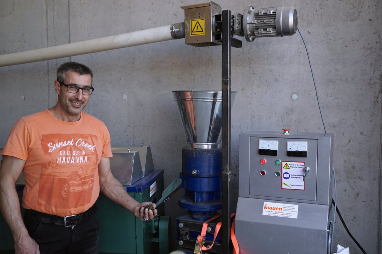 Legehennen-Halter Ruedi Huber mit Pellets in der Hand vor der Pelletier- und Trocknungsmaschine. Bild: Michael Götz