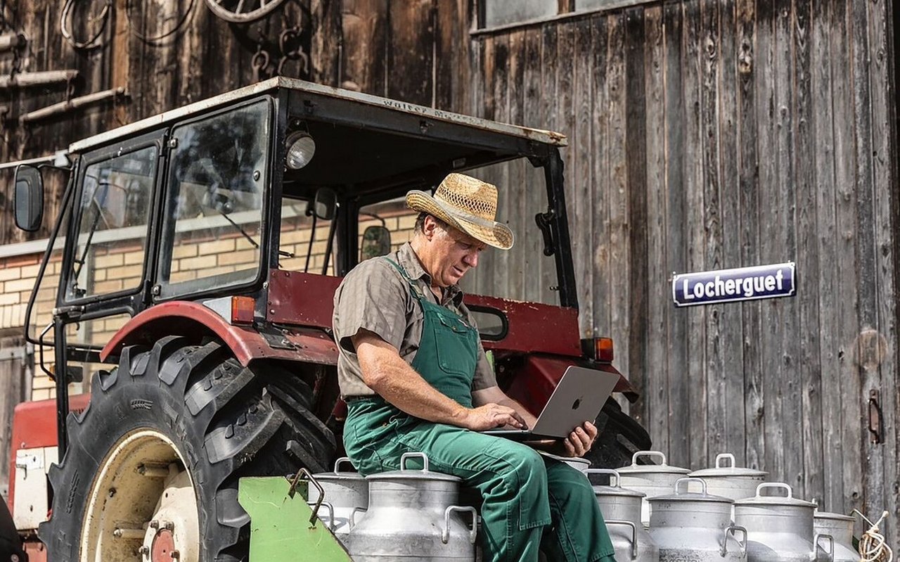 Landwirt sitzt auf Milchkannen und schreibt auf einem Notebook.