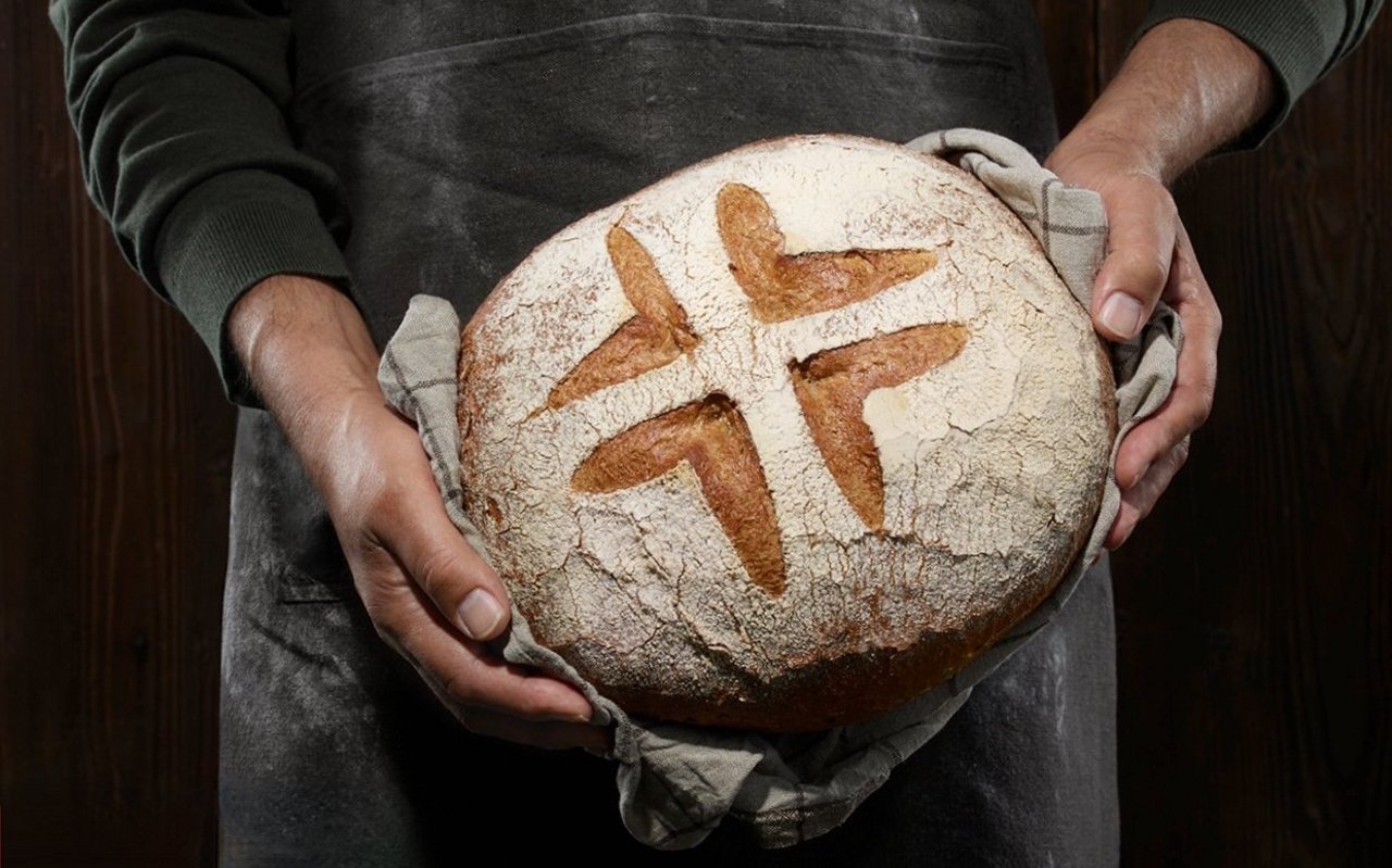 Ein Bäcker hält einen Brotlaib mit dem Schweizer-Brot-Logo in den Händen.