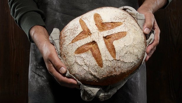 Ein Bäcker hält einen Brotlaib mit dem Schweizer-Brot-Logo in den Händen.