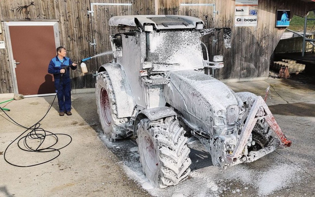 Ein Mann sprüht den Traktor mit weissem Schaum voll.