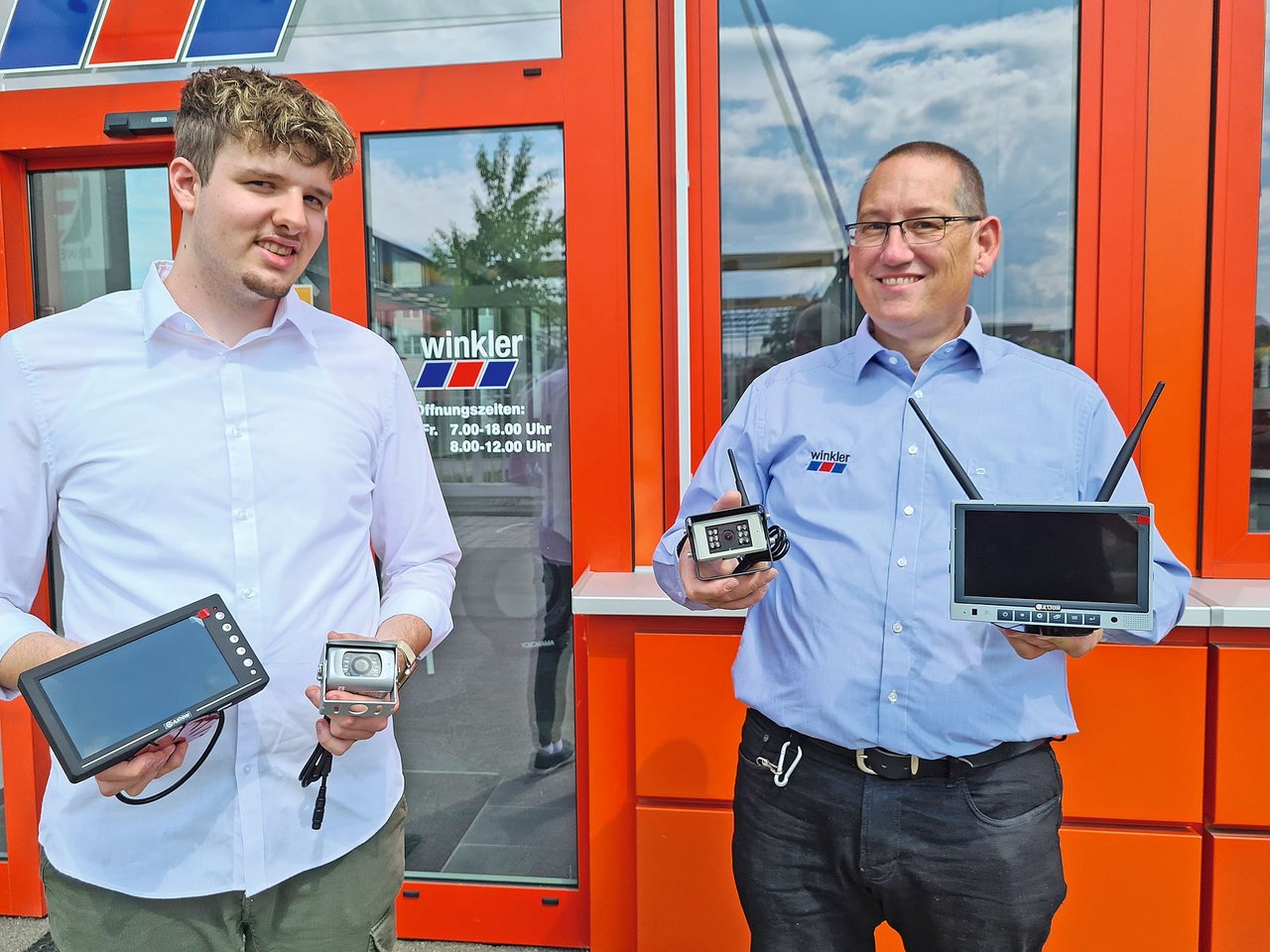 Sie halten die Teile einer Rückfahr-Überwachungskamera in den Händen. Patrick Fuchs (links) mit einer kabelgebundenen Lösung und Daniel Arnold mit Kamera und Bildschirm mit Antenne für die Funkübertragung. Bild: Bild: die grüne/Beat Schmid