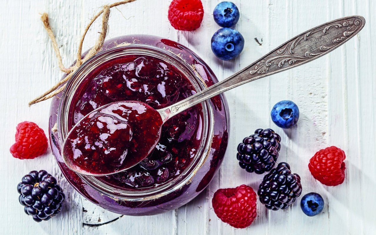 Himbeeren, Brombeeren und Heideleeren neben einem Glas Konfitüre.