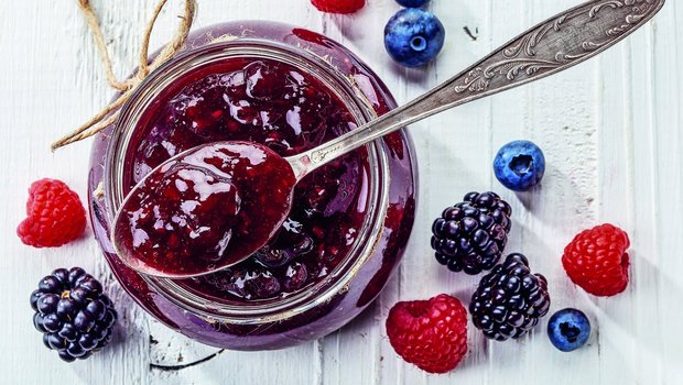 Himbeeren, Brombeeren und Heideleeren neben einem Glas Konfitüre.