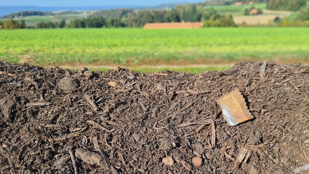 An einer Kompostmiete am Feldrand sind diverse Verpackungen und Fitzelchen von Plastik zu sehen.