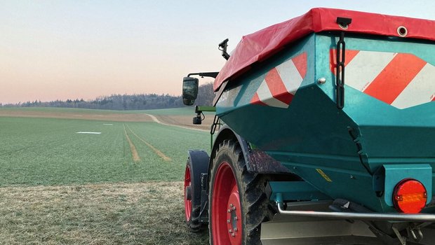ein Traktor mit angehängtem Düngerstreuer steht am Rand eines Weizenfelds.