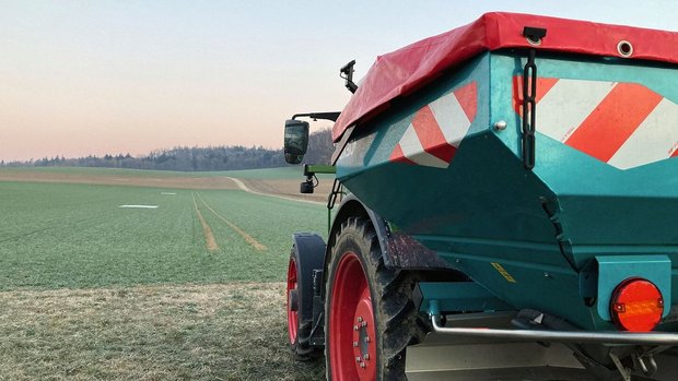 Smart-N: Stickstoffdünger optimieren ein Traktor mit angehängtem Düngerstreuer steht am Rand eines Weizenfelds.